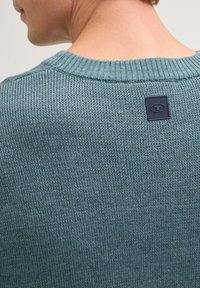 Strickpullover in Tiefblau mit einem gerippten Ausschnitt und einem strukturierten Muster. Verfügt über ein schwarzes Logo-Patch auf der Rückseite nahe dem Kragen.