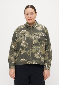 Veste courte à motif floral vert avec des clous argentés sur le col et les poches. Fabriquée en tissu texturé avec des manches longues.