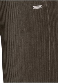 Brown corduroy fabric with vertical ribbing, featuring a small metallic tag labeled "TASCGANA." The texture appears soft and plush.