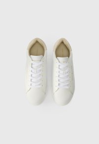 Baltas ādas sporta apavi ar baltiem zābakiem, noapaļota purngala un gluda tekstūra. Iekšējā oderē ir beige krāsa un diskrēta zelta zīmola identifikācija.