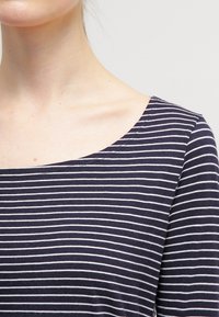 Granatowo-biały top w paski z szerokim dekoltem typu łódka i krótkimi rękawami, wykonany z miękkiej tkaniny o gładkiej fakturze.