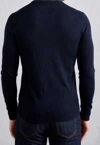 Mörkblå tröja med långa ärmar, rund hals, ribbad nederkant och slät textur. Bärs med mörka denimjeans.