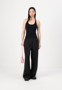 Top negru fără mâneci și pantaloni negri largi. Modelul ține o geantă mică roz. Culori solide, design simplu, croială relaxată.