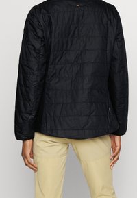 Černá prošívaná bunda s texturovanou tkaninou, dlouhými rukávy, kulatým výstřihem a bočními kapsami, spárovaná se světle béžovými kalhotami.