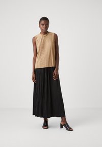 Beige plisserte ermeløs topp kombinert med en lang svart plisserte skjørt; modellen har på seg svarte åpne tå mules. Glatt tekstur, fremtredende vertikale linjer.