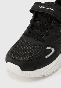 Μαύρο και άσπρο παπούτσι Champion με διχτυωτή μύτη, συνθετικά επικαλύμματα, κορδόνια και ιμάντα βέλκρο στο πάνω μέρος.