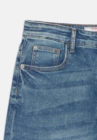 Blaue Denim-Jeans mit mittelhohem Bund, Fünf-Taschen-Design, Akzenten aus Nähten und einer dezenten, verblassten Textur.