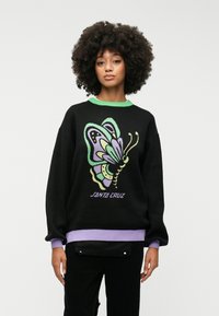 Sweater preto com um design de borboleta colorida, gola verde, punhos roxos e o texto "SANTA CRUZ" na parte inferior. Textura suave.