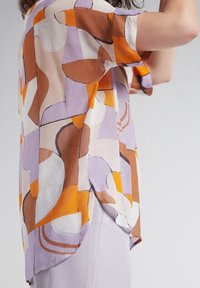 Chemise à manches courtes présentant un motif abstrait coloré dans des tons d'orange, marron, lilas et crème. Tissu léger avec une coupe décontractée.