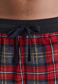 Pantalons de pyjama en polaire avec un motif écossais rouge, bleu et jaune. Dotés d'une ceinture élastique noire avec un cordon à nouer.