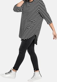 Musta-valkoraidallinen pitkähihainen paita pyöreällä helmalla, yhdistetty mustiin kapealahkeisiin farkkuihin ja valkoisiin korkeavartisiin lenkkareihin.