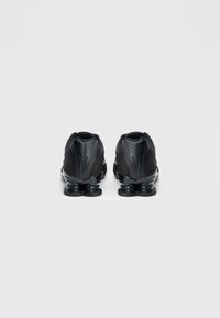 Czarne buty sportowe z chropowatą tkaniną na wierzchu, z wyrazistymi liniami, amortyzowaną czarną gumową podeszwą oraz zaokrąglonym tyłem.