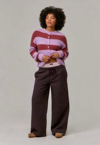 Cardigan riscado em rosa e lavanda, com botões e mangas caneladas. Combinado com calças largas castanhas escuras com cordão.