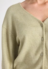 Lichtgroene gebreide cardigan met een diepe V-hals, lange mouwen en vier knoopsluitingen aan de voorkant. Zachte textuur en een ontspannen pasvorm.