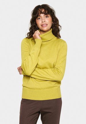 Felpa a collo alto verde lime realizzata in morbido tessuto knit, con maniche lunghe e orlo a coste, abbinata a pantaloni marroni scuri.