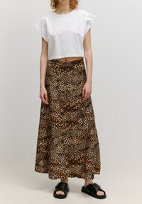 Witte cropped t-shirt met brede mouwen, gecombineerd met een lange bruine midi-rok met luipaardprint en zwarte platte sandalen. Zachte stoftextuur.