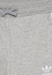 Šedé bavlněné tepláky s texturovaným povrchem, které mají elastický pás a šňůrku na stažení. Bílé logo Adidas potisknuté na dolní části nohavice.