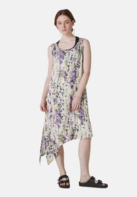Rochie asimetrică dintr-un material ușor, cu o bază albă și un model tie-dye în nuanțe de violet și verde. Fără mâneci, cu decolteu rotund, asortată cu sandale negre.
