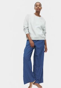 Felpa grigio chiaro con scollo rotondo e maniche lunghe abbinata a pantaloni pigiama larghi a quadri blu e neri. Vestibilità comoda, tessuto morbido.