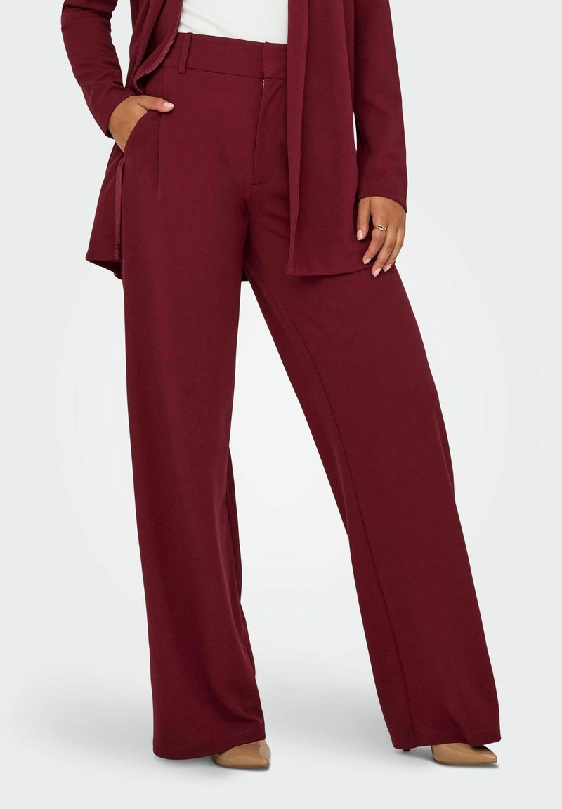 Pantalones de pernera ancha en burdeos, confeccionados con una tela suave. Cuentan con bolsillos delanteros y una cintura ajustada. Combinados con una camiseta blanca.