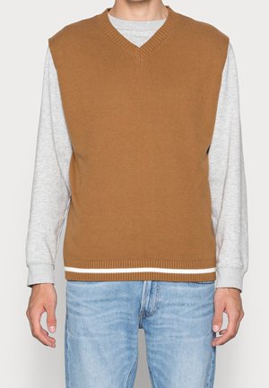 V-kaulushihna, ilmanhihaista neuletta ruskeasta ribbikudoksesta, kerroksittain vaaleanharmaan pitkähihaisen paidan päällä. Valmis valkoisilla raitakujilla.