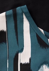 Tejido con un patrón en verde azulado y blanco con acentos en negro, que presenta un estilo de arte urbano texturizado, combinado con un fondo de algodón negro.