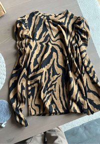 Top con stampa zebra marrone e nera, con maniche lunghe, tessuto morbido, scollatura rotonda e dettagli arricciati sulle spalle.