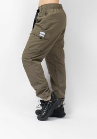 Olijfgroene cargobroek met een elastische tailleband, zijzakken en een verstelbare trekkoord. Gestyled met zwarte schoenen en gemusterde sokken.