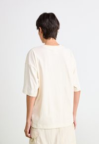 Kremfarget oversized t-skjorte med korte ermer, laget av bomull, minimalistisk design, flate sømdetaljer på halslinning og nederkant.