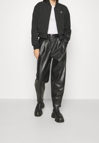 Czarna pikowana kurtka bomberka z prążkowanymi mankietami i zamkiem błyskawicznym z przodu, zestawiona z czarnymi spodniami z wysokim stanem z sztucznej skóry oraz masywnymi czarnymi butami.