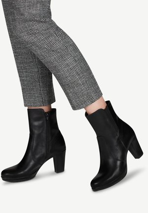 Bottines en cuir noir avec un bout arrondi, des zips sur les côtés et un talon bloc de hauteur moyenne, assorties à un pantalon à motif pied-de-poule gris.