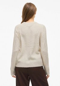 Suéter de punto acanalado beige con mangas largas y escote redondeado. Textura suave, corte ligeramente corto y dobladillo deshilachado.