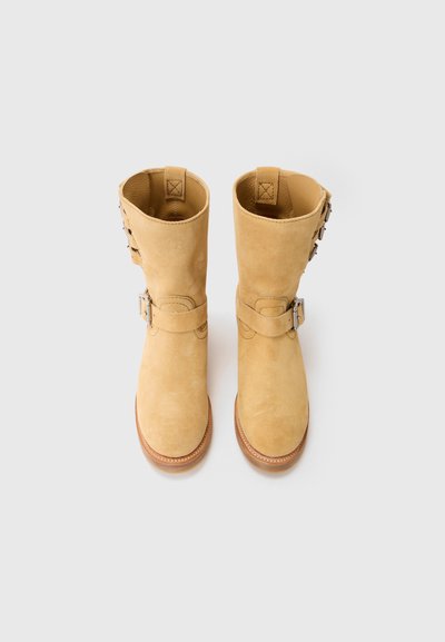 Botas de tobillo de ante en color marrón claro con una textura suave, que cuentan con una correa y detalle de hebilla, y una puntera redondeada. Suela de goma resistente y acentos cosidos.