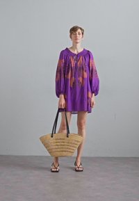 Lyhyt violetti mekko, jossa on puffihihat ja oranssi kukkakuosi. Malli pitää suurta kudottua olkikassia, jossa on mustat kahvat.