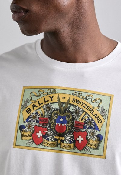 Camiseta blanca con un colorido logo de Bally de Suiza, decorado con acentos florales, formas de escudo y diseños intrincados.