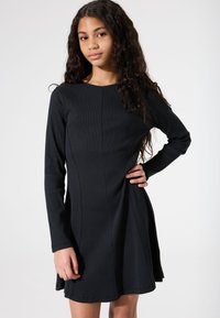 Schwarzes langärmeliges Kleid mit enganliegendem Oberteil und ausgestelltem Rock, aus strukturiertem Rippenstoff gefertigt. Verfügt über Nahtdetails an der Vorderseite.