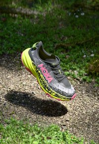 Hoka löparskor i grått och svart med neongula accenter. Tjock dämpad sula, texturerad ovandel och framträdande rosa logotyp.