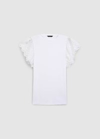 T-shirt blanc avec encolure arrondie et manches courtes, orné de détails en dentelle complexe le long des bords, créant un effet superposé avec des volants.