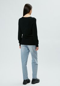 Un pull noir en tricot avec un ourlet côtelé, associé à un jean droit bleu clair et des chaussures à plateformes noires, vu de dos.