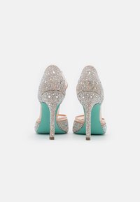 Sandali con tacco alto con base nuda, adornati con strass trasparenti e una suola turchese. La vista posteriore mette in risalto gli intricati embellishments e la forma.