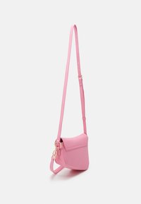 Petit sac bandoulière rose avec bandoulière ajustable et anneaux en métal doré, présenté suspendu sur fond blanc uni.