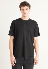 Black cotton t-shirt with a crew neck, short sleeves, and a small white Calvin Klein logo on the chest. Smooth texture and relaxed fit.