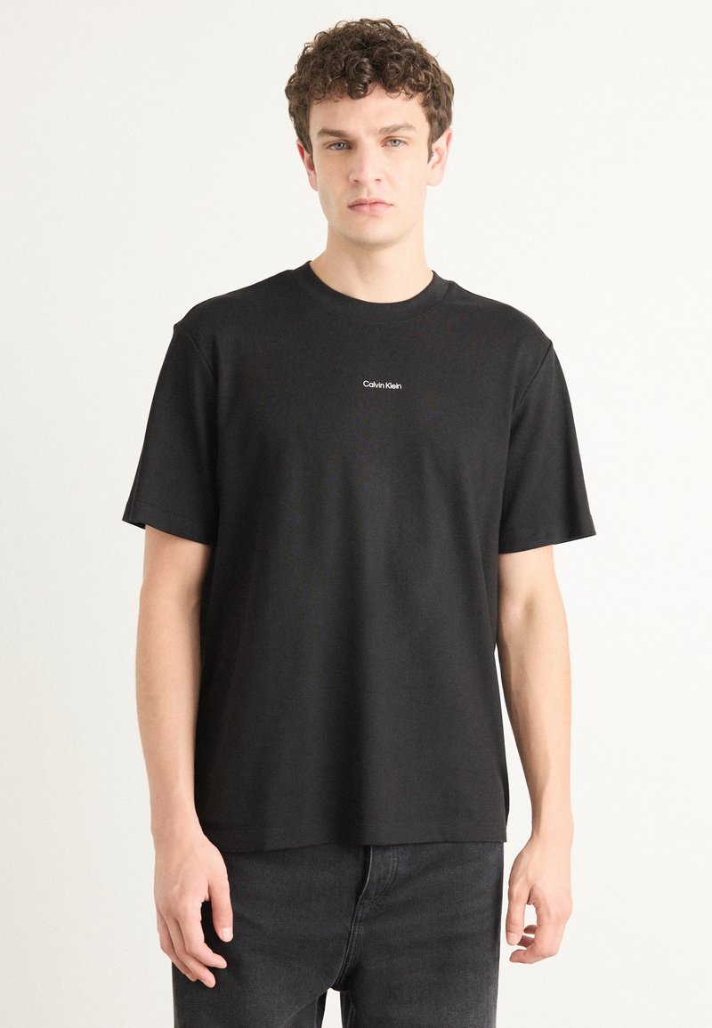 Black cotton t-shirt with a crew neck, short sleeves, and a small white Calvin Klein logo on the chest. Smooth texture and relaxed fit.