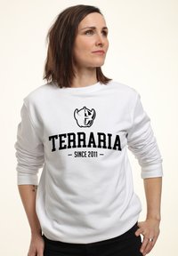 Bílá mikina s kulatým výstřihem, na které je černý logo "TERRARIA" s textem "SINCE 2011." Dlouhé rukávy a uvolněný střih.