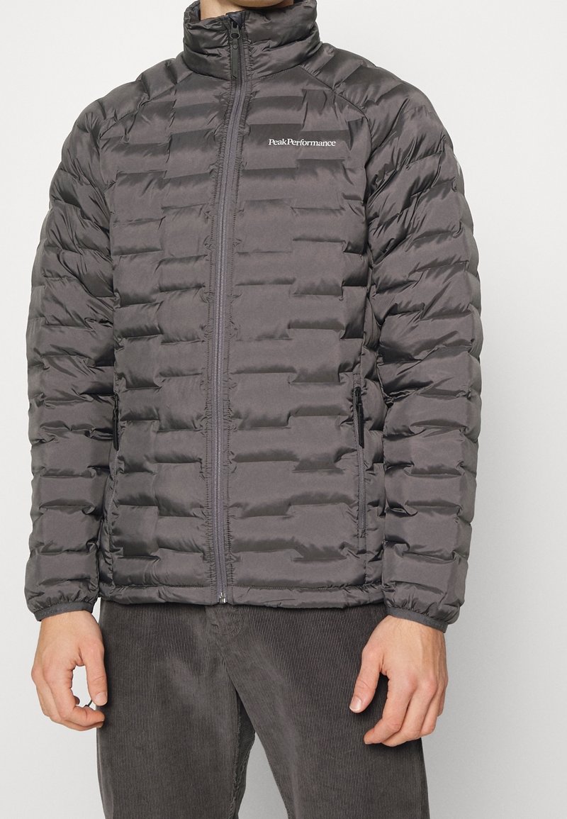 Giacca puffer grigia scura con zip frontale, colletto alto, design trapuntato e logo del marchio discreto sul petto. Tessuto morbido e liscio.