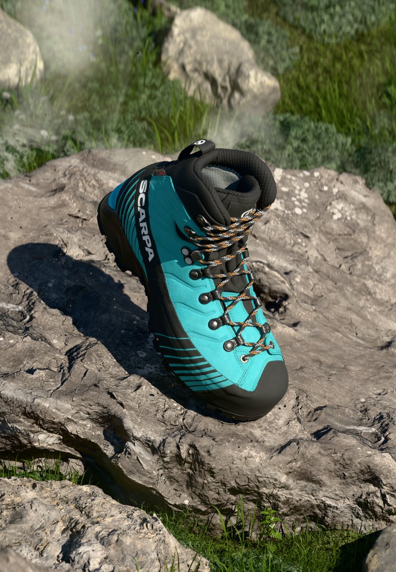 Botas de caminhada SCARPA em teal e preto com atacadores laranja, descansando em terreno rochoso, com erva verde ao fundo.