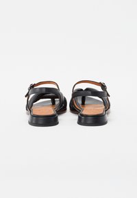 Sandalias de cuero negro con parte superior texturizada, talón abierto y correa ajustable con hebilla; con una plantilla acolchada marrón y suela baja negra.