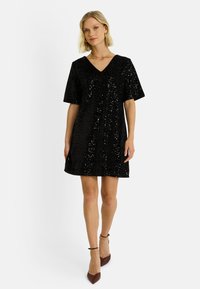 Robe à paillettes noires avec un décolleté en V, des manches courtes et une silhouette en A. Texture lisse et détail de surface scintillant.