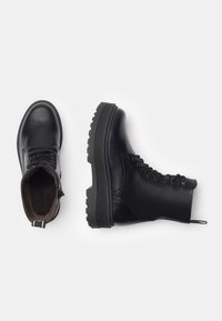 Schwarze Lederstiefeletten mit runder Zehenform, Schnürverschluss und robuster Gummisohle mit strukturiertem Muster. Seitlicher Reißverschluss für einfaches An- und Ausziehen.