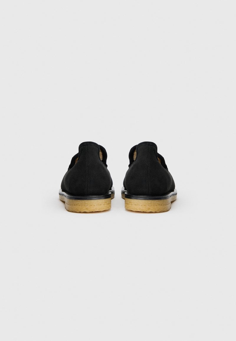 Scarpe nere in suede con il retro basso, suola in gomma beige e dettagli di cucitura discreti. Il design è minimalista senza ulteriori accenti.